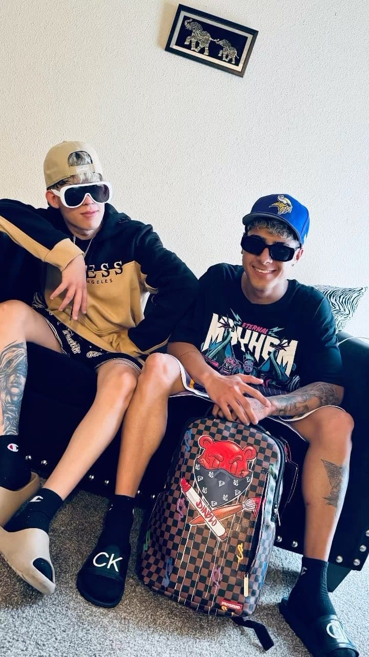 Milian y un amigo sentados en un sofá junto a una maleta de viaje estampada