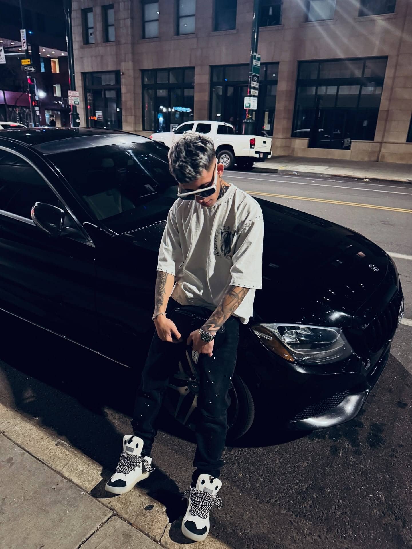 Milian de pie junto a un coche negro en una calle del centro