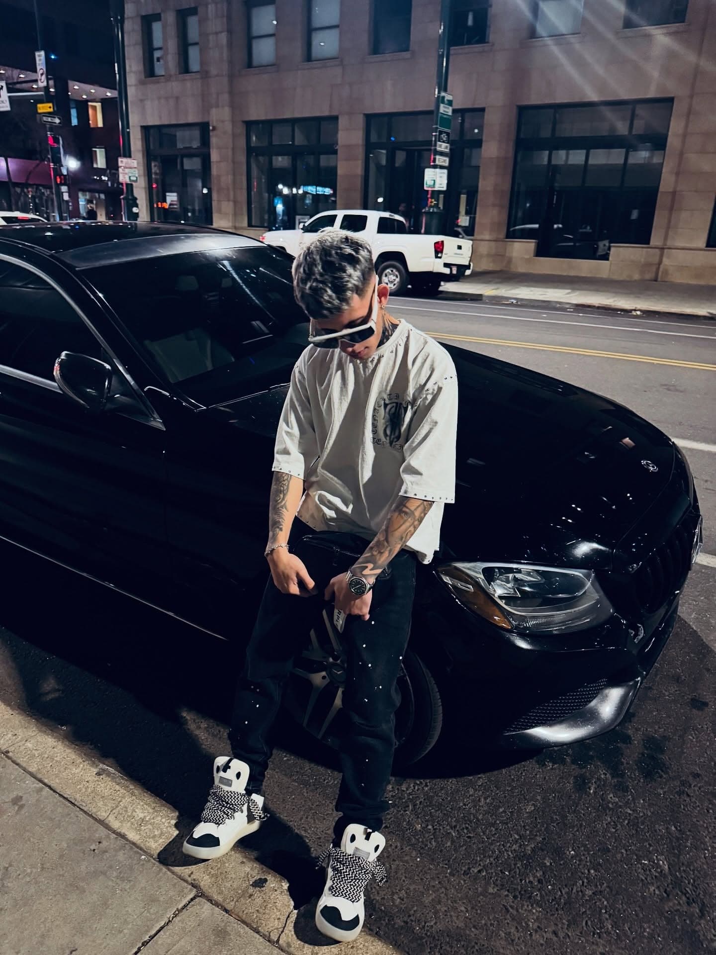 Milian de pie junto a un coche negro en una calle del centro