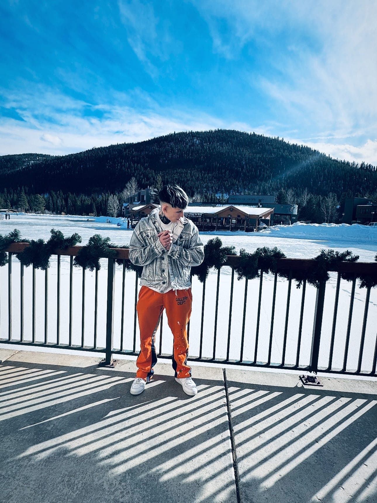 Milian apoyado en una barandilla frente a un lago helado y montañas nevadas
