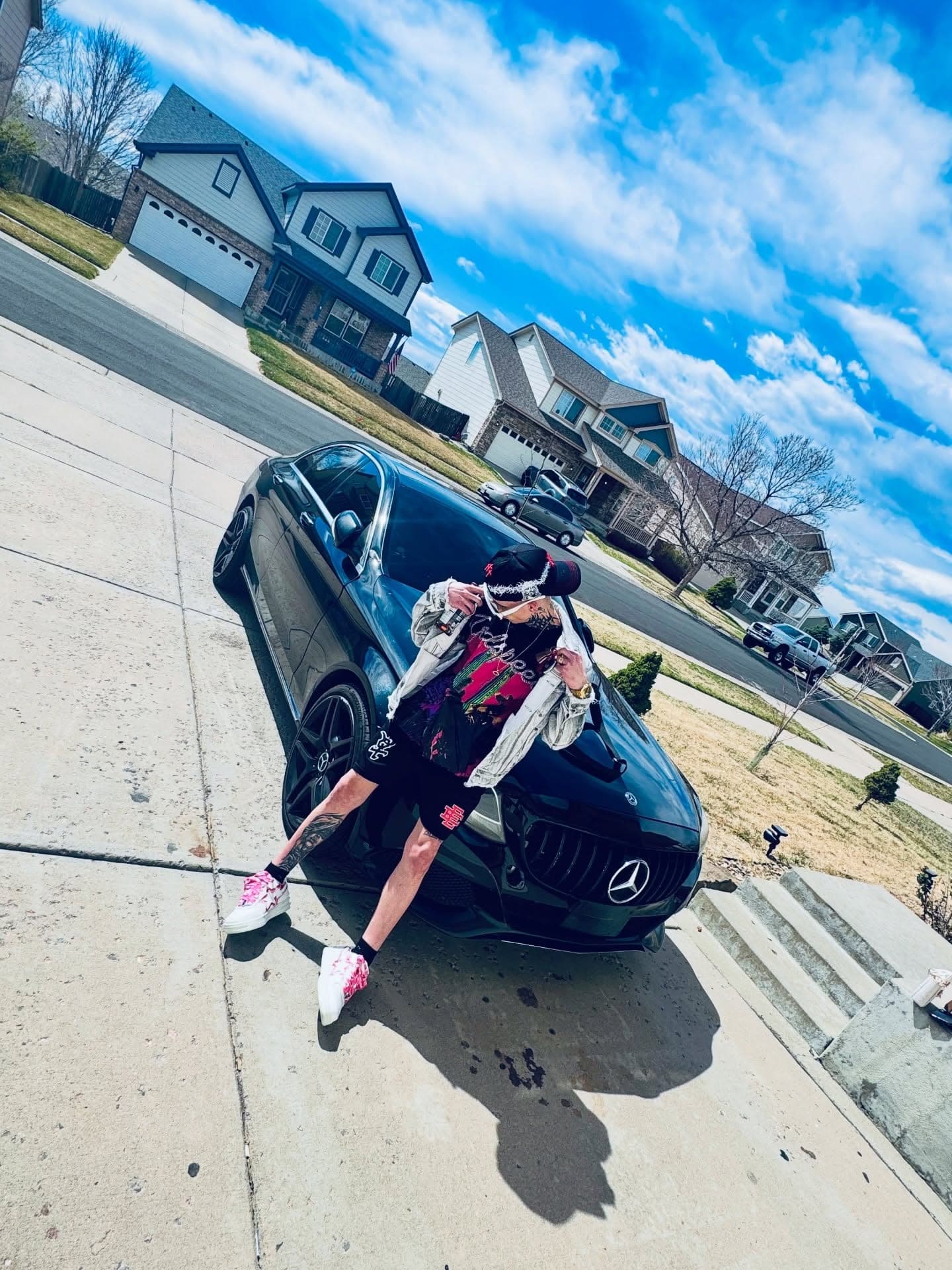 Milian sentado en el capó de un Mercedes negro en un barrio residencial de Denver